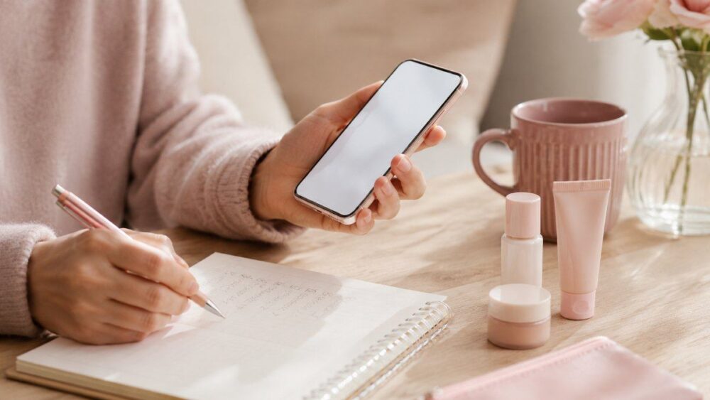 スマホを見ながら買い物リストを書く女性の手元